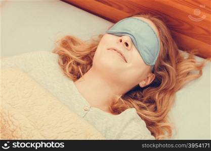 Tired woman sleeping in bed wearing blindfold sleep mask. Young girl taking nap.