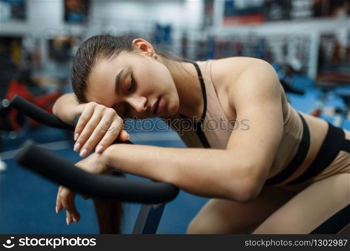 Tired woman sleeps on a stationary bike in gym. People on fitness workout in sport club, athletic girls in sportswear on training indoors. Tired woman sleeps on a stationary bike in gym