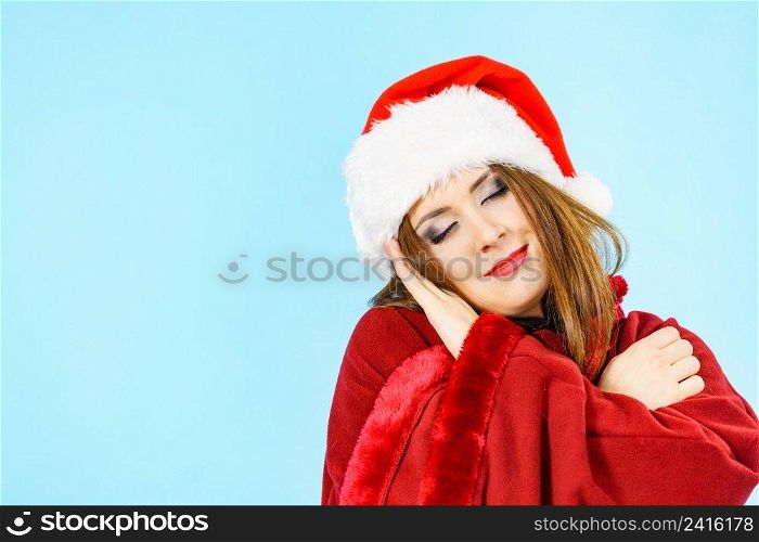 Tired woman wearing santa hat gesturing sleep gesutre with her hands. Adult female being sleepy, ready to take a nap. Christmas time.. Woman in santa hat being sleepy