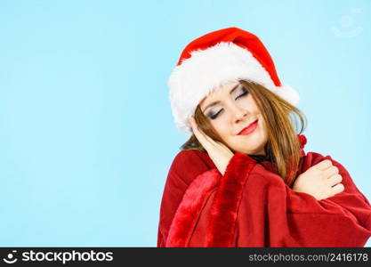 Tired woman wearing santa hat gesturing sleep gesutre with her hands. Adult female being sleepy, ready to take a nap. Christmas time.. Woman in santa hat being sleepy