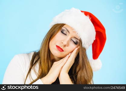 Tired woman wearing santa hat gesturing sleep gesutre with her hands. Adult female being sleepy, ready to take a nap. Christmas time.. Woman in santa hat being sleepy