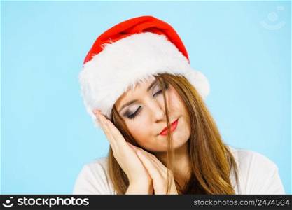 Tired woman wearing santa hat gesturing sleep gesutre with her hands. Adult female being sleepy, ready to take a nap. Christmas time.. Woman in santa hat being sleepy