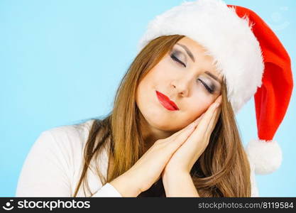 Tired woman wearing santa hat gesturing sleep gesutre with her hands. Adult female being sleepy, ready to take a nap. Christmas time.. Woman in santa hat being sleepy