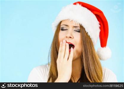 Tired woman wearing santa hat yawning. Adult female being sleepy, ready to take a nap. Christmas time.. Woman in santa hat being sleepy