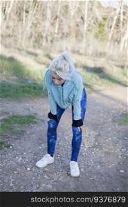 Tired young blonde woman with hands on knees after jogging