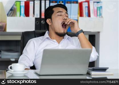 tired young businessman using laptop and yawning