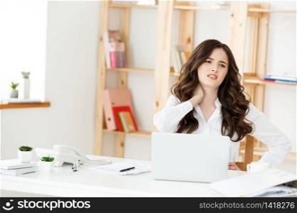 Tired young businesswoman suffering from long time sitting at computer desk in office.. Tired young businesswoman suffering from long time sitting at computer desk in office
