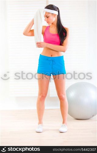 Tired young girl at living room wiping her face with towel after exercising&#xA;