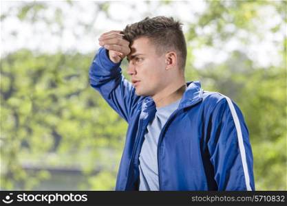 Tired young man wiping sweat after jogging at park