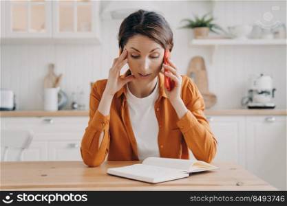 Tired young woman is remote employee. Girl is working from home sitting at the table and talking on telephone. Secretary, office manager or customer support assistant. Workspace at home concept.. Tired young woman is remote employee working from home. Secretary or office manager.
