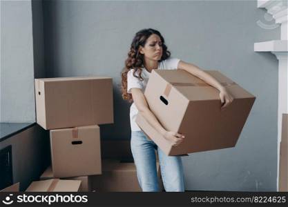 Tired young woman renter exhausted of carrying heavy cardboard boxes with things on moving day. Upset hispanic girl tenant frowning leaving rented apartment. Mortgage, real estate tenancy concept. Tired female tenant carrying box with things leaving rented apartment. Eviction, hard relocation day