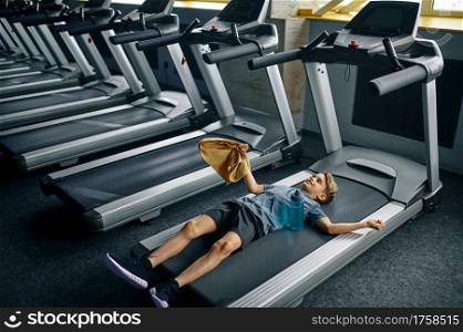 Tired youngster lying on treadmill in gym, running machine. Boy on training, health care and healthy lifestyle, schoolboy on workout. Tired youngster lying on treadmill in gym