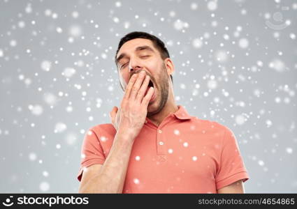 tiredness, bedtime, winter, christmas and people concept - tired yawning man over snow on snow background