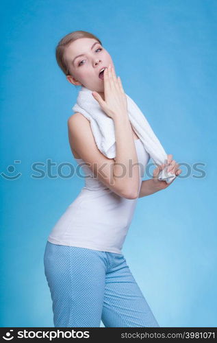 Tiredness, boredom concept. Sleepy woman placing hand on mouth yawning while holding towel on shoulder, studio shot on blue background. Bored sleepy woman yawning while holding towel