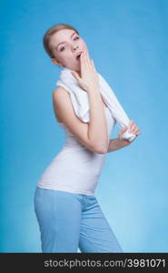 Tiredness, boredom concept. Sleepy woman placing hand on mouth yawning while holding towel on shoulder, studio shot on blue background. Bored sleepy woman yawning while holding towel