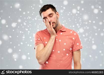 tiredness, stress, winter, christmas and people concept - tired sleepy young man over snow on gray background