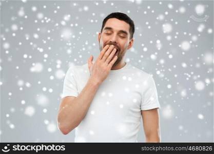 tiredness, winter, christmas and people concept - tired yawning man over snow on gray background