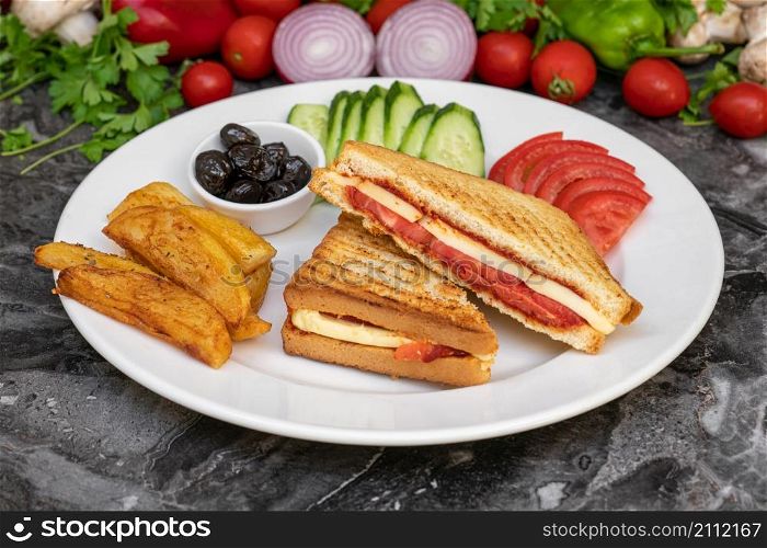 Toast with cheddar cheese, sausage and tomato with french fries and salad on marble table