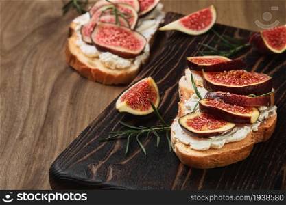 Toast with figs and cream cheese on a wooden board for serving, closeup view, selective focus. Snack idea, before dinner. Close-up on healthy food