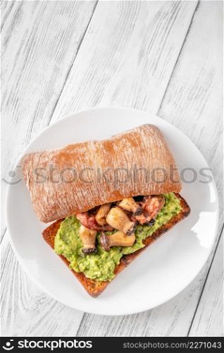 Toast with guacamole, mushrooms and bacon on white plate