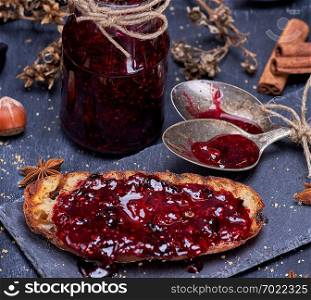 toast with raspberry jam and empty jam jar with an iron spoon on a black background