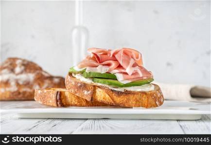 Toast with slices of avocado, prosciutto and cream cheese