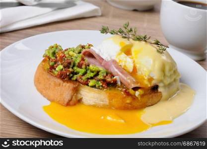 Toasted baguette slice with guacamole, ham and eggs Benedict under Dutch sauce