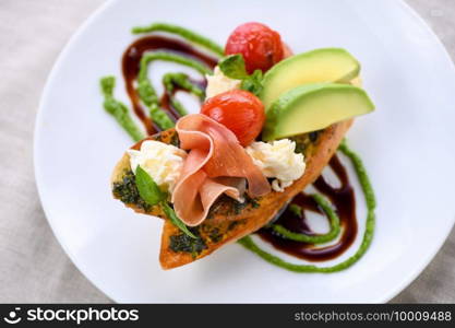 Toasted baguette toast with pesto sauce, a slice of Parma ham, mozzarella, tomato and avocado