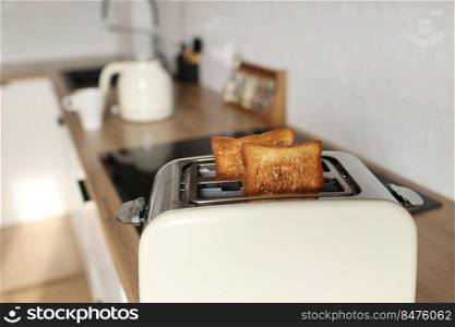 Toasted bread and toaster for breakfast. Modern white toaster and roasted bread slices toasts inside on wooden table in kitchen. Toasted bread and toaster for breakfast. Modern white toaster and roasted bread slices toasts inside on wooden table in kitchen.