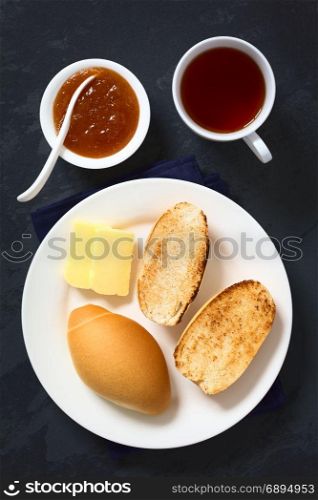 Toasted bread rolls with butter, peach jam and tea on the side, photographed overhead on slate with natural light. Bread Rolls with Jam and Tea