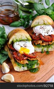 Toasted ciabatta with pesto, slices of bacon, sun-dried tomatoes and poached egg