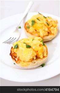 Toasted muffins topped with scrambled egg garnished with chopped mint on a plate with a fork.