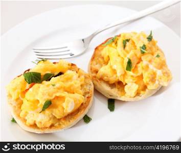 Toasted muffins topped with scrambled egg garnished with chopped mint on a plate with a fork.