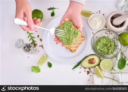 Toasts preparation - woman smearing mashed avocado on a toasted bread.. Toasts preparation - woman smearing mashed avocado on a toasted bread