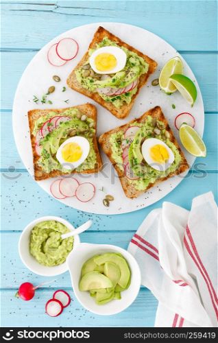 Toasts with avocado guacamole, fresh radish, boiled egg, chia and pumpkin seeds. Diet breakfast. Delicious and healthy plant-based food. Flat lay. Top view