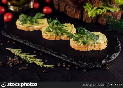 Toasts with avocado guacamole on black wood