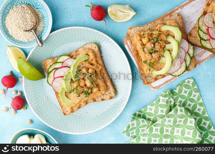 Toasts with chickpea hummus, avocado, fresh radish, cucumber, sesame seeds and flaxseed sprouts. Diet breakfast. Delicious and healthy plant-based vegetarian, vegan food. Flat lay. Top view