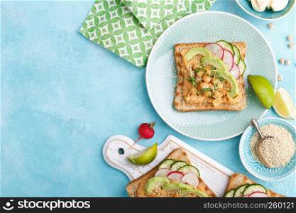 Toasts with chickpea hummus, avocado, fresh radish, cucumber, sesame seeds and flaxseed sprouts. Diet breakfast. Delicious and healthy plant-based vegetarian, vegan food. Flat lay. Top view