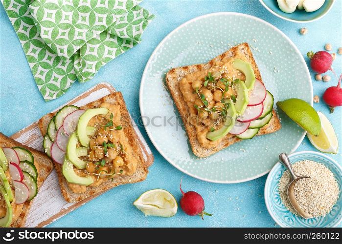 Toasts with chickpea hummus, avocado, fresh radish, cucumber, sesame seeds and flaxseed sprouts. Diet breakfast. Delicious and healthy plant-based vegetarian, vegan food. Flat lay. Top view