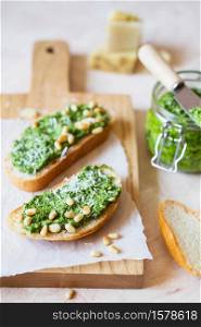 Toasts with traditional Italian basil pesto sauce on a light grey stone table. Green pesto with pine nuts and parmesan.