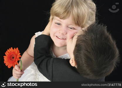 Toddler boy giving young girl a kiss on the cheek. Shot in studio over black.