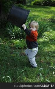 Toddler boy holding a large planter pot over his head in the back yard