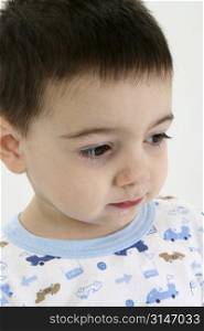 Toddler boy in pajamas with runny nose and drool on face. Sad expression, circles under eyes. Shot in studio.