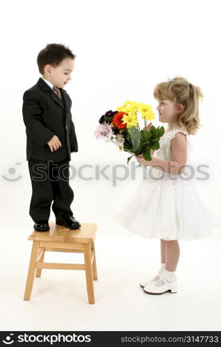 Toddler boy in suit giving flowers to pretty little girl in pageant dress.