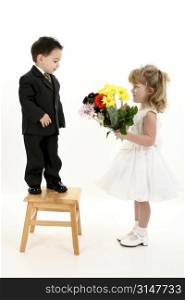 Toddler boy in suit giving flowers to pretty little girl in pageant dress.