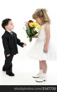 Toddler boy in suit giving flowers to pretty little girl in pageant dress.