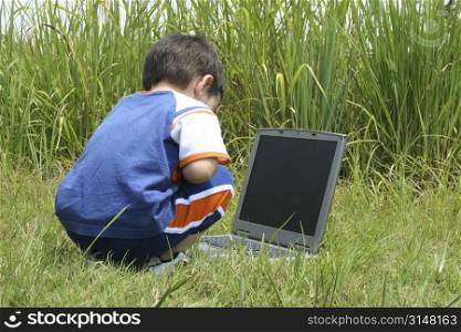 Toddler boy looking at laptop in tall grass.