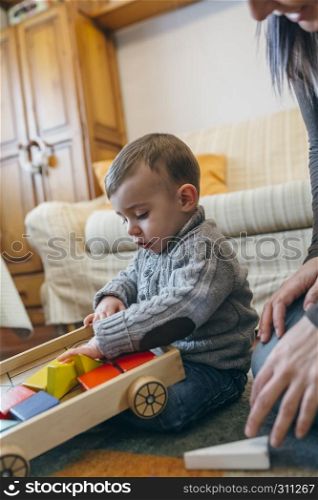 Toddler boy playing with a wooden game building in the living room. Toddler boy playing with a wooden game building