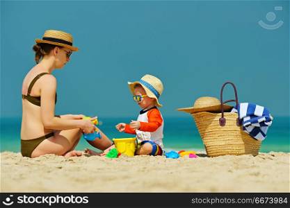 Toddler boy playing with mother on beach . Two year old toddler boy in sun hat playing with mother on beach