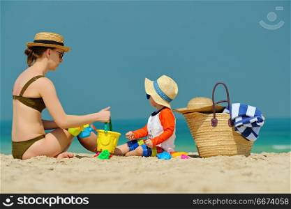 Toddler boy playing with mother on beach . Two year old toddler boy in sun hat playing with mother on beach